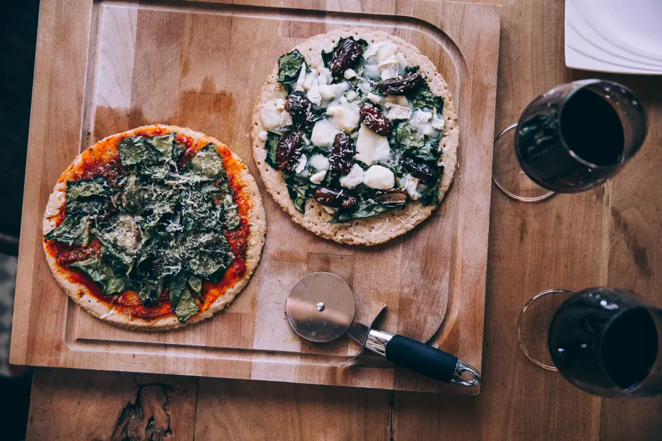 Two pizzas on a board with red wine