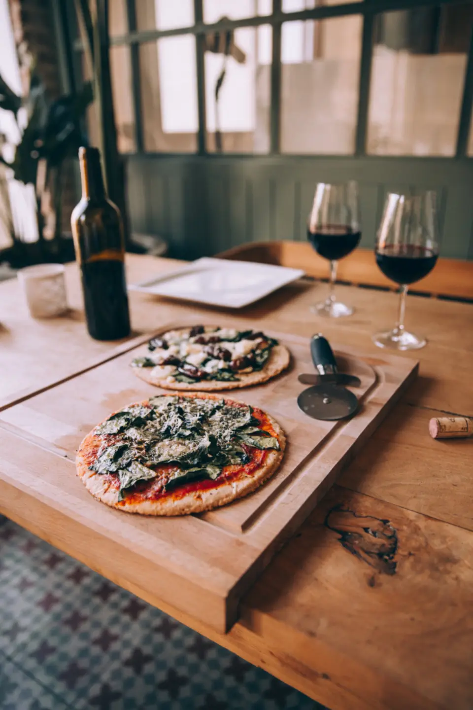 Pizzas, wine and a pizza cutter on a table